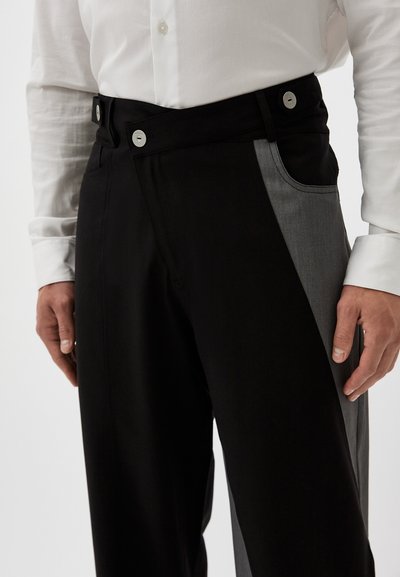 Schwarze und graue Patchwork-Hosen mit glatter Textur, ausgestattet mit zwei silbernen Knöpfen und einer seitlichen Taschenakzentuierung.