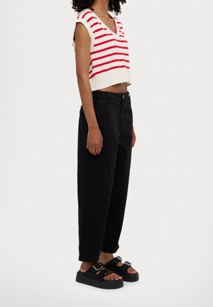 Femme portant un haut court sans manches blanc à rayures rouges, un pantalon noir taille haute et des sandales plateformes noires avec deux boucles.