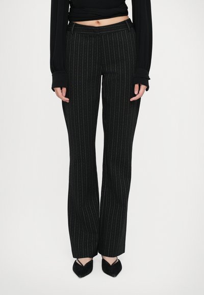 Schwarze gestreifte Hosen mit taillierter Passform, die am Saum einen leichten Schlag aufweisen und eine glatte Textur haben. Getragen mit schwarzen spitzen Ballerinas.