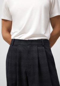 Gepreste donkergrijze broek met een gestructureerde stof, voorzien van een platte tailleband en zijzakken, gecombineerd met een eenvoudige witte t-shirt.