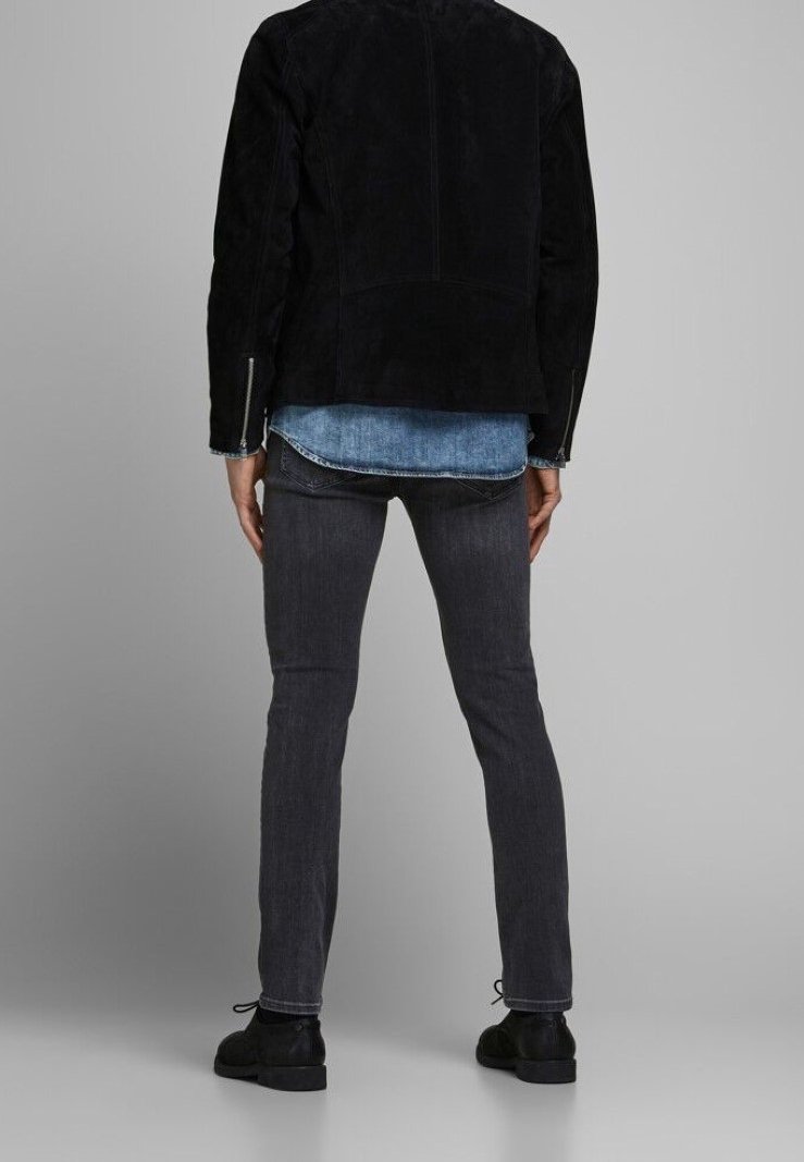 Giacca in camoscio nero a taglio dritto, indossata sopra una camicia di jeans. Jeans aderenti grigio scuro e scarpe nere completano il look.