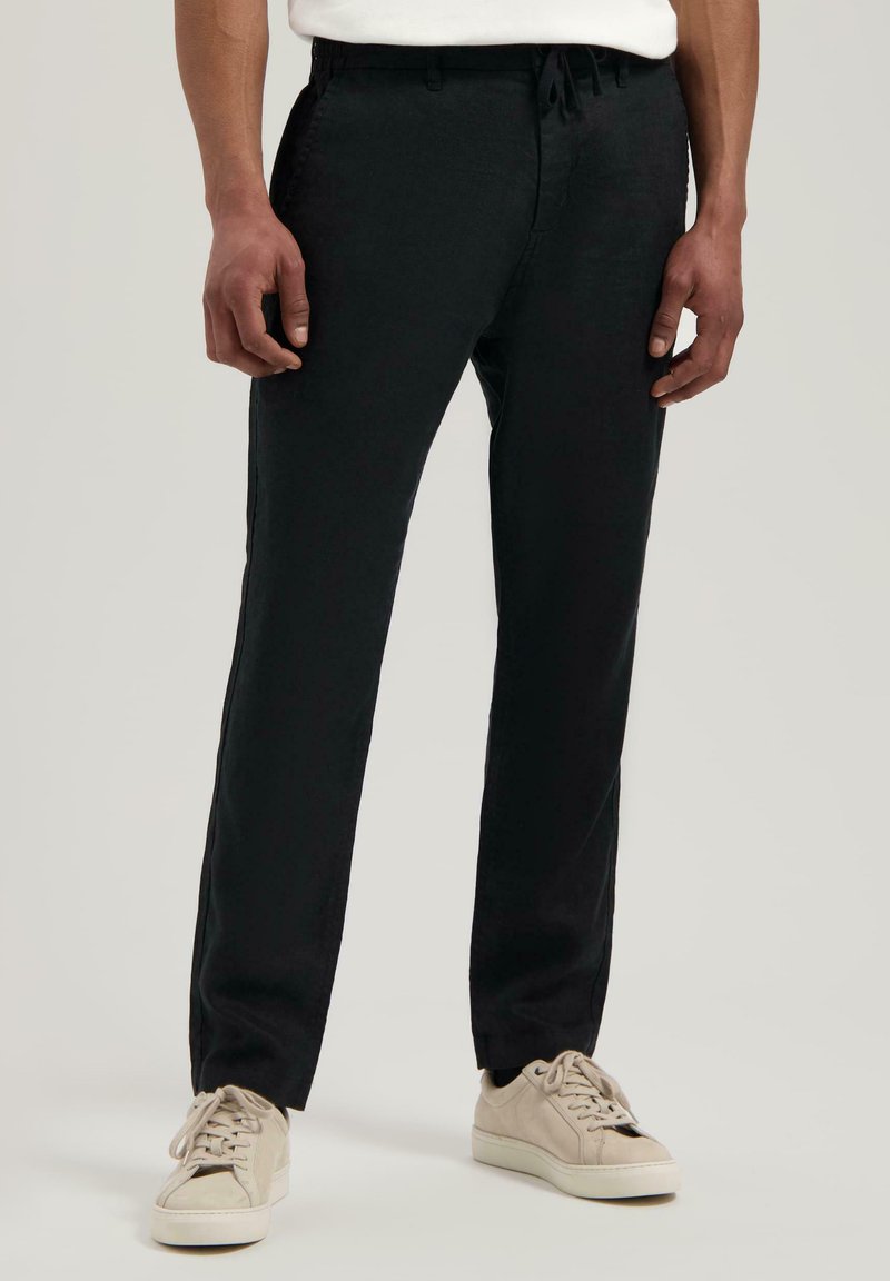 Pantaloni neri leggeri con vita regolabile; design a gamba dritta; indossati con sneakers di colore chiaro. Texture liscia.