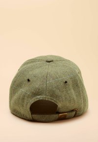 Șapcă de tip baseball verde, din lână, cu textură în model chevron, curea ajustabilă și accent metalic. Vedere din spate care arată orificiile pentru ventilație.