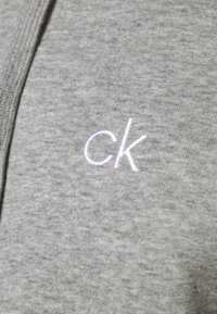 Felpa grigia realizzata in morbido tessuto, con un piccolo logo "ck" ricamato in bianco sul petto. Design semplice senza motivi o accenti visibili.