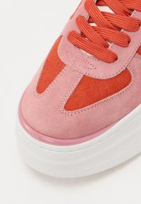 Rosa semskesko med oransje detaljer, med teksturerte overlegg, rund tå og kontrasterende røde lisser. Hvit gummisåle med merkevare.