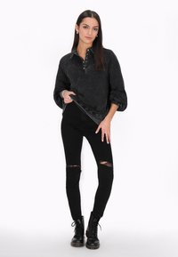 Černý oversized svetr s texturovaným povrchem a zapínáním na knoflíky, spárovaný s černými roztrhanými skinny džíny a černými šněrovacími botami.