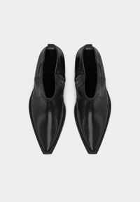 Ζευγάρι κομψών μαύρων αμυγδαλωτών δερμάτινων μποτάκια αστραγάλου με πλαϊνό φερμουάρ και θηλιά, φωτογραφημένα από πάνω σε λευκό φόντο.