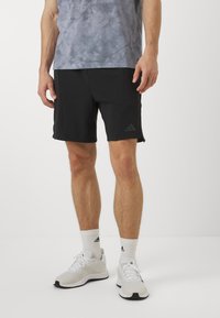 Shorts de sport noirs avec une texture lisse et des fentes sur les côtés. Associés à un t-shirt gris à motif tie-dye et des baskets blanches avec des accents noirs.
