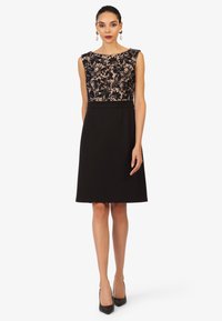 Robe noire avec un corps en dentelle à motifs floraux, design sans manches et jupe évasée. Agrémentée de plis discrets.