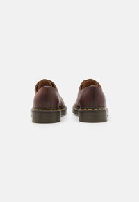Braune Lederschuhe mit runder Zehenform und niedrigem Absatz, die eine auffällige gelbe Naht entlang der Sohle und eine glatte Textur aufweisen.