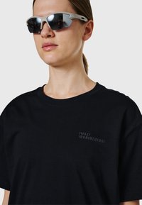 Femme portant des lunettes de sport réfléchissantes et un t-shirt noir avec le texte « HALO 1968|972|981 » sur la poitrine.
