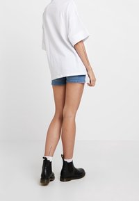Botas negras de cuero hasta el tobillo con un acabado suave y tacón pequeño, combinadas con shorts de mezclilla y una camiseta blanca oversized y holgada.