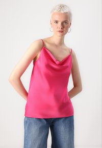 Rosa satin camisole med en bølget hals og tynne stropper, med en glatt og blank tekstur. Kombinert med lyseblå denimshorts.