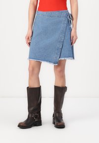 Denim omslagskjørt i lyseblått med frynset kant og sidesnor, kombinert med kne-høye brune lærstøvler med spenne-detaljer.