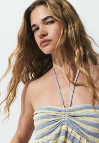 Top sin tirantes, de múltiples rayas en azul claro y amarillo. Presenta fruncidos y delgadas tiras de halter. Textura viva y suave.