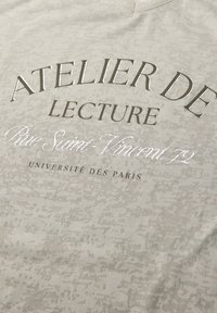 Texto en tela gris claro que dice "Atelier de Lecture, Rue Saint-Vincent 72, Université des Paris" en fuentes variadas y con impresión metálica.