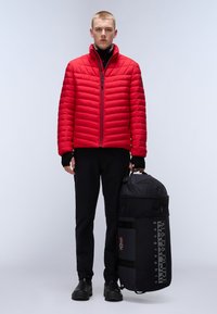Rød quiltet jakke med lynlås, sort turtleneck, sorte bukser og sort bæretaske med logo og flagdetaljer.
