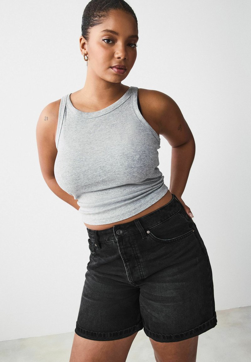 Camiseta de tirantes gris con canalé y pantalones cortos de mezclilla negros de cintura alta, con un ajuste ceñido, dobladillo enrollado y cierre de botón frontal.