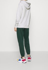 Sudadera con capucha gris, pantalones jogger verdes y zapatillas coloridas con acentos en azul, amarillo y rosa, y lunares, vistas desde atrás.