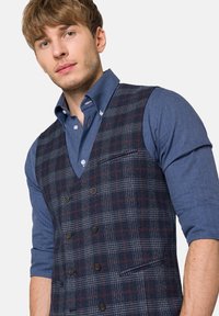 Marynarski, w kratkę, kamizelka o podwójnym zapięciu, z guzikami oraz kieszenią na piersi, noszona na niebieskiej koszuli z guzikami.