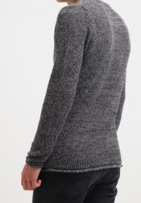 Grau gestrickter Pullover mit strukturiertem Muster, ausgestattet mit langen Ärmeln und Rundhalsausschnitt, kombiniert mit dunklen Jeans.