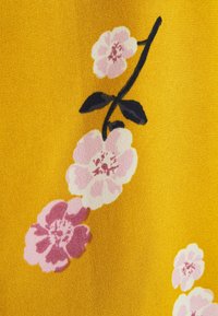 Tissu jaune avec des motifs floraux en nuances de rose et blanc, accompagné de feuilles vert foncé, présenté avec une finition texturée.