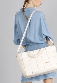 Borsa tote bianca intrecciata con un design strutturato, realizzata in pelle, dotata di doppi manici e di una tracolla removibile. Accento con logo dorato visibile.