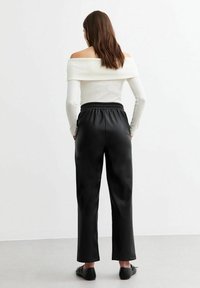 Svarta konstläderbyxor med avslappnad passform, elastisk midja och raka ben. Kombineras med en figurnära långärmad topp i off-white.