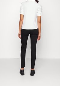 Polo shirt bianco a coste abbinato a pantaloni neri slim-fit, con una texture liscia e dettagli minimi. Scarpe con tacco nere completano il look.