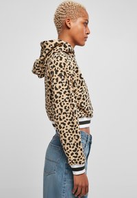 Kuttet hettegenser i tan med svart leopardmønster. Har snor i hetten og ribbestrikkede mansjetter med svart og hvitt stripe. Brukt med høyt liv bukser.