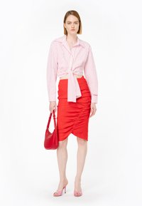 Camicetta bianca tagliata con righe rosse, legata in vita; gonna rossa arricciata; sandali con tacco rosa; borsa rossa con tracolla.
