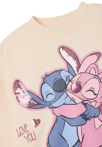 Sudadera crema con una gran impresión colorida de dos personajes de dibujos animados abrazándose, decorada con lentejuelas rosas y el texto "TE QUIERO."
