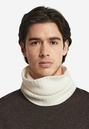 Biała, fakturowana golf z dzianiny. Noszona na ciemnym, teksturowanym swetrze. Zbliżenie na obszar szyi, podkreślające detale i wzór.