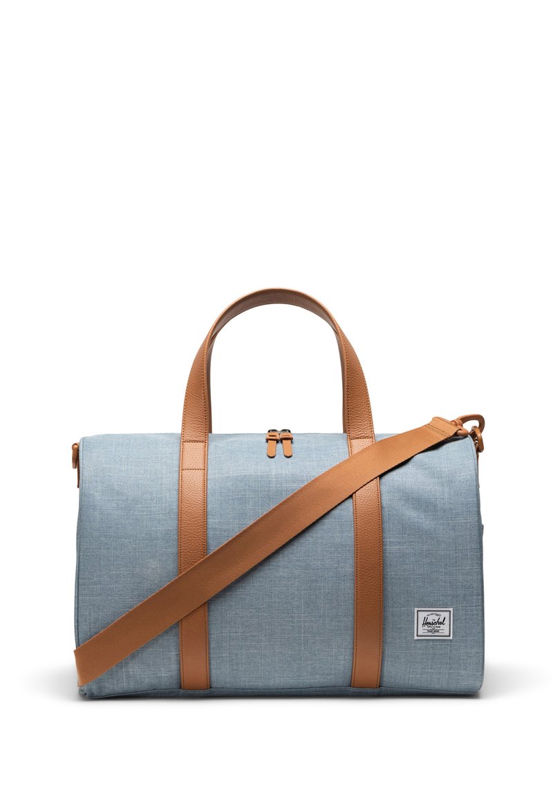 Cestovná taška svetlomodrej farby z látky s hnedými syntetickými koženými popruhmi, ktorá má horné zapínanie na zips a malú nášivku s logom značky.