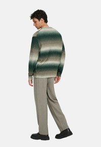 Pull en tricot avec un dégradé de vert et de brun, col rond, poignets côtelés, associé à un pantalon beige et des chaussures noires.