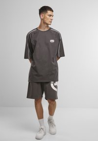 Grå oversized t-shirt med hvide sidelister og logo på brystet, parret med matchende shorts med hvid grafiktryk. Hvide sneakers.