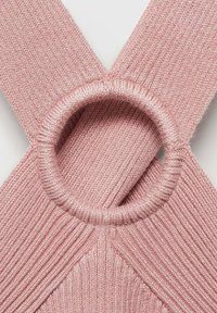 Pleteni roza top z rebrasto teksturo, ki vsebuje krožni poudarek, kjer se srečata naramnici, in oblikuje V-obliko na hrbtu.