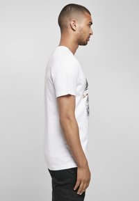 Weißes Baumwoll-T-Shirt mit grafischem Druck auf der Vorderseite, kurzen Ärmeln und Rundhalsausschnitt, kombiniert mit schwarzen Hosen.