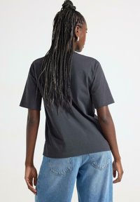 Mørkegrå kortærmet t-shirt med en afslappet pasform, der har en rund halsudskæring og en glat bomuldsstruktur, stylet med blå denim jeans.