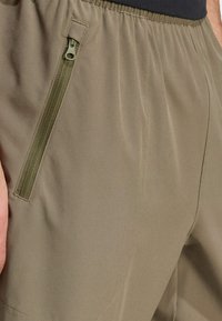 Lys olivengrønne shorts med en glat tekstur, der har en skrå lynlåslomme på højre side og elastisk talje.