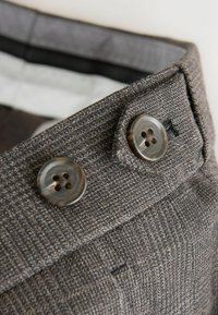 Tissu gris texturé avec un motif subtil, présentant deux grands boutons ronds foncés sur la ceinture et une doublure intérieure lisse.