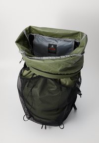 Mochila verde con un exterior texturizado, bolsillo frontal de malla, forro gris y herrajes negros; cuenta con un cierre superior ajustable.