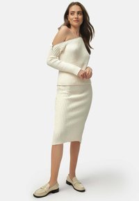 White ribbed knit sweater with off-the-shoulder design, paired with a matching knee-length ribbed skirt. Beige loafers complete the outfit.