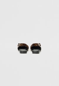 Leopard-print flat sandals with an open back, textured upper, and sleek black soles. Features a single strap across the foot.