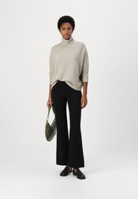 Beige stickad turtleneck-sweater, svarta utsvängda byxor, svarta loafers, hållande en grön handväska. Enkelt mönster, mjuk textur, avslappnad passform.