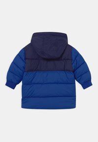 Chaqueta puf azul con capucha, que presenta un diseño a bloques de color en azul marino oscuro y azul brillante, puños acanalados y textura acolchada.