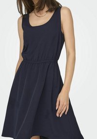 Robe sans manches bleu marine avec un décolleté arrondi, taille froncée, jupe fluide et texture douce ; design minimaliste sans motifs visibles.