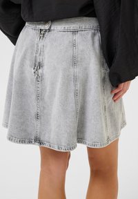 Gonna di jeans in grigio chiaro, con chiusura a zip, design svasato e dettagli di cucitura a vista. Il tessuto ha una consistenza morbida.