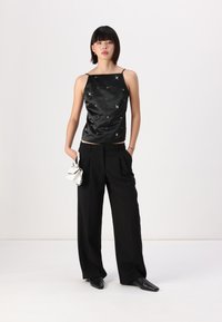Black satin sleeveless top with scattered embellishments, paired with high-waisted black trousers and sleek black pointed shoes.