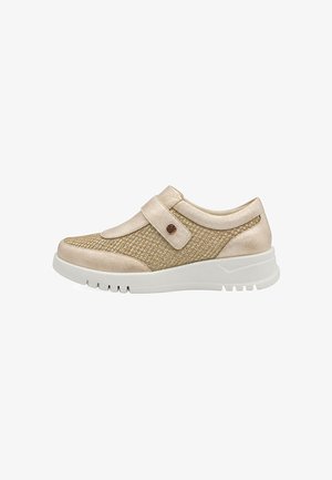 Zapato casual beige claro con lados de malla texturizada, una correa ancha con detalle de botón y suela blanca gruesa.